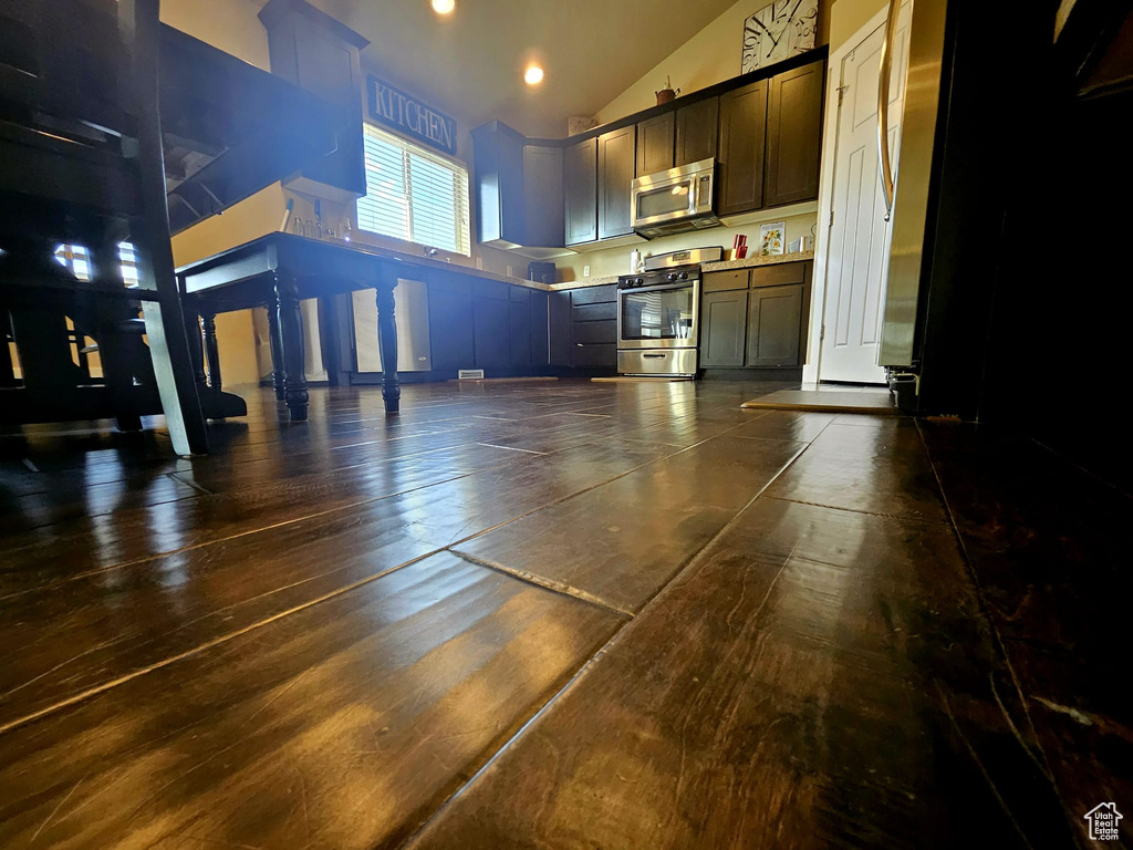 Kitchen featuring stainless steel appliances, high vaulted ceiling, light countertops, and dark brown cabinets