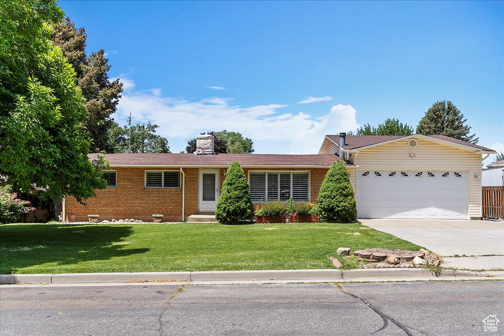 Ranch-style house with an attached garage, concrete driveway, brick siding, a front yard, and a chimney