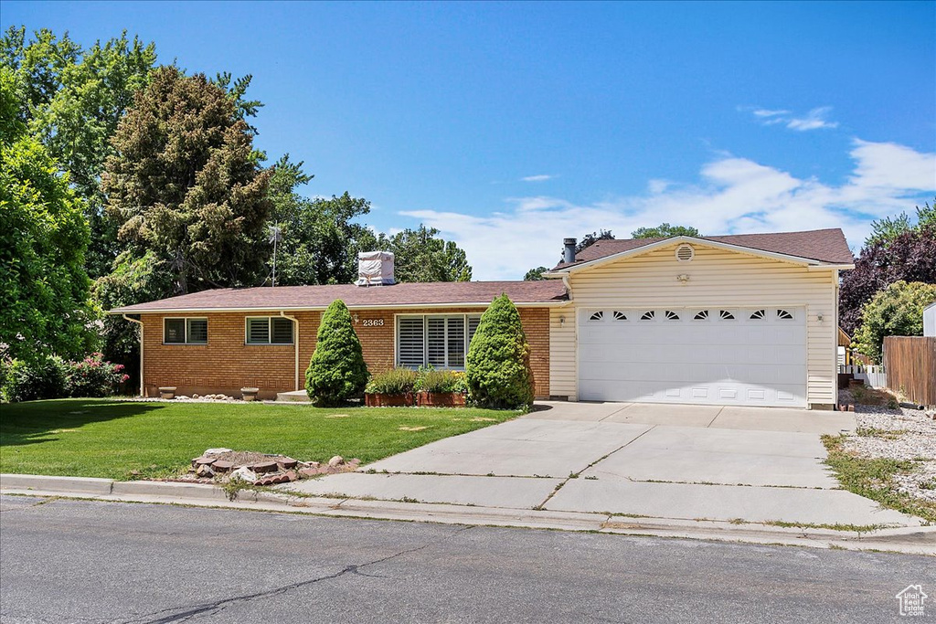 Single story home with a garage, concrete driveway, a front yard, and brick siding
