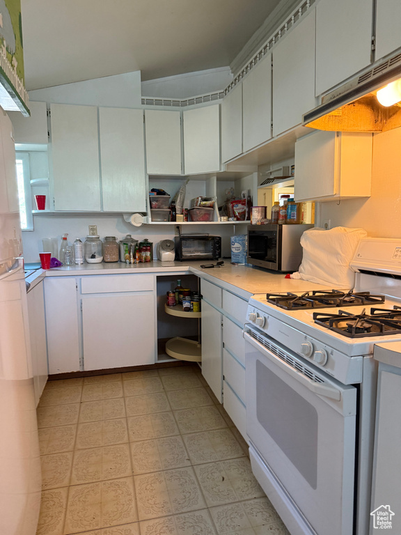 Kitchen with white gas stove, stainless steel microwave, light countertops, and under cabinet range hood