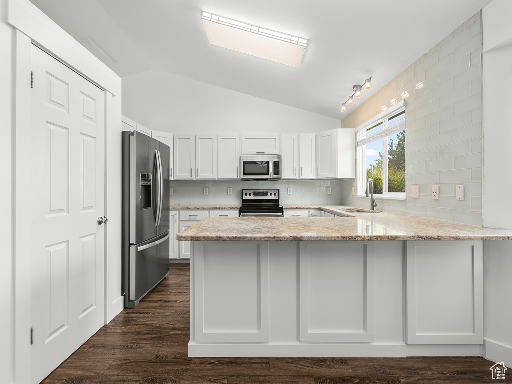 Kitchen featuring appliances with stainless steel finishes, a peninsula, vaulted ceiling, white cabinetry, and backsplash
