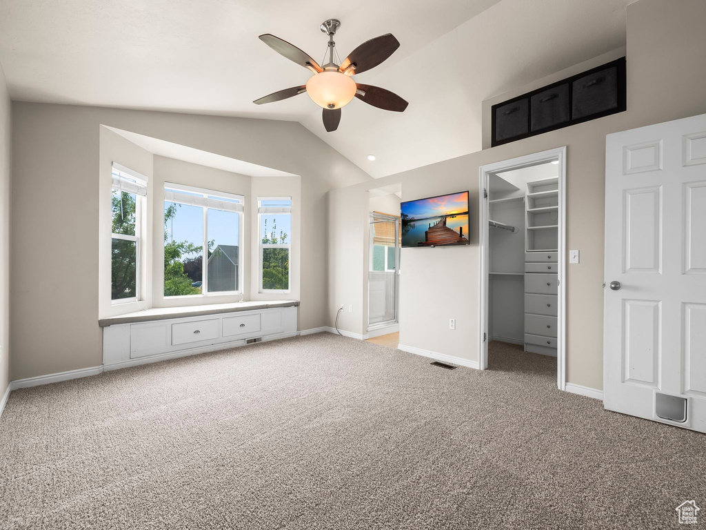 Unfurnished bedroom with carpet floors, a walk in closet, lofted ceiling, a closet, and ceiling fan