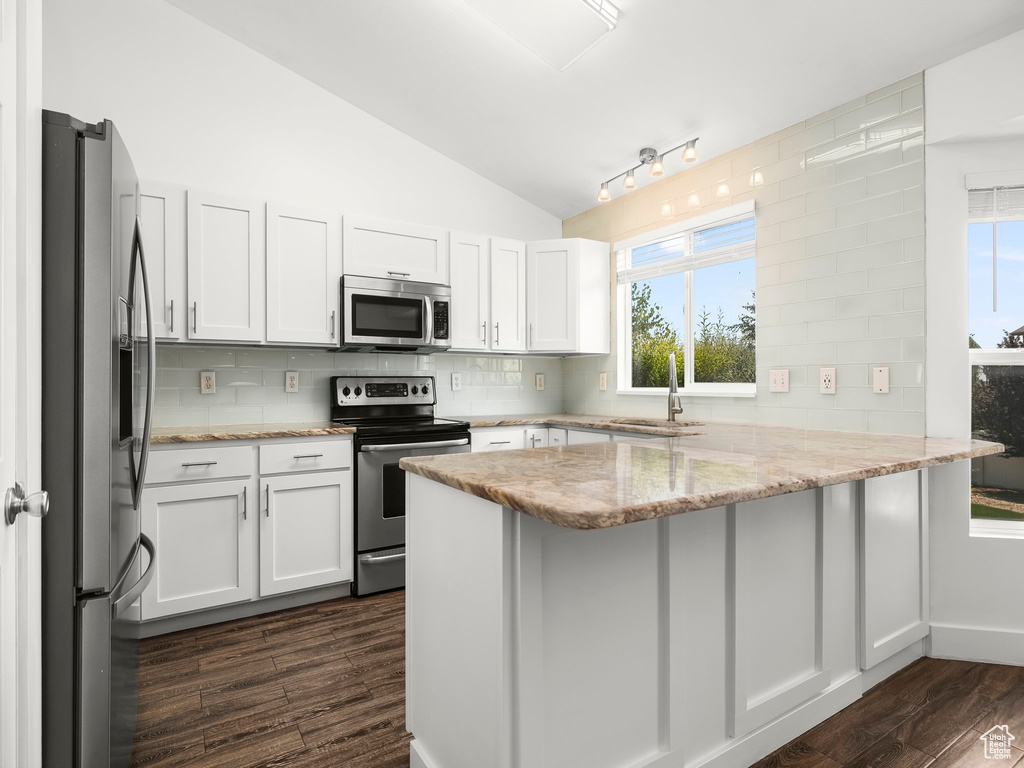 Kitchen with stainless steel appliances, a peninsula, dark wood-style flooring, decorative backsplash, and white cabinetry