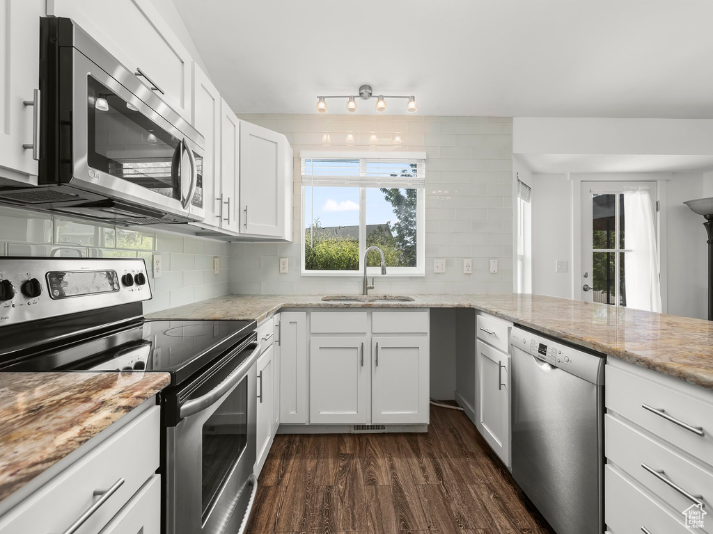 Kitchen featuring appliances with stainless steel finishes, dark wood-type flooring, tasteful backsplash, white cabinetry, and light stone counters