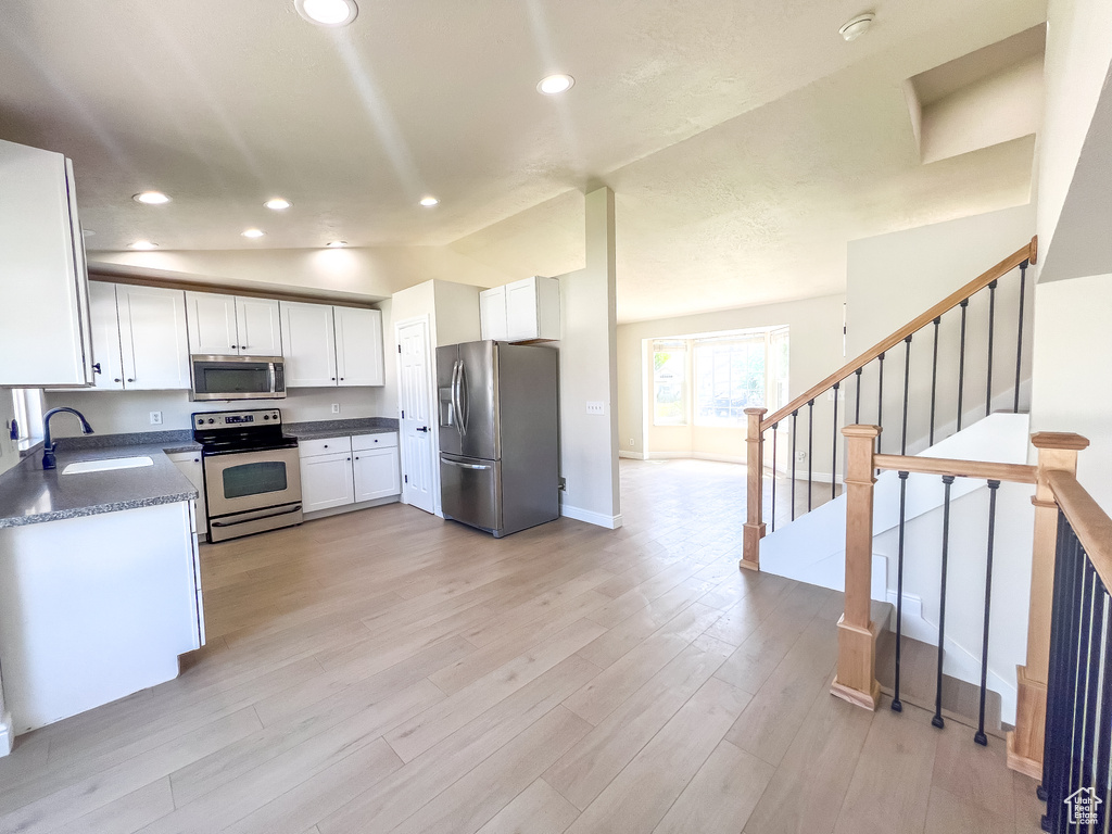 Kitchen featuring appliances with stainless steel finishes, dark countertops, white cabinets, recessed lighting, and light wood-style flooring