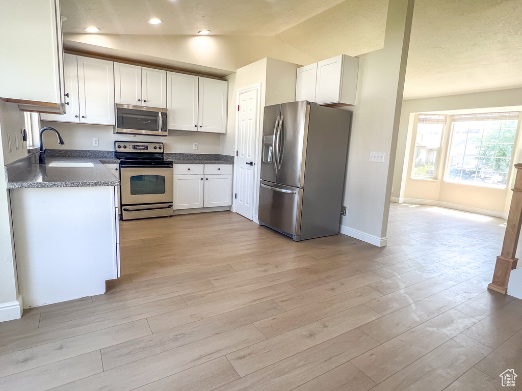 Kitchen with appliances with stainless steel finishes, white cabinetry, dark countertops, light wood finished floors, and recessed lighting
