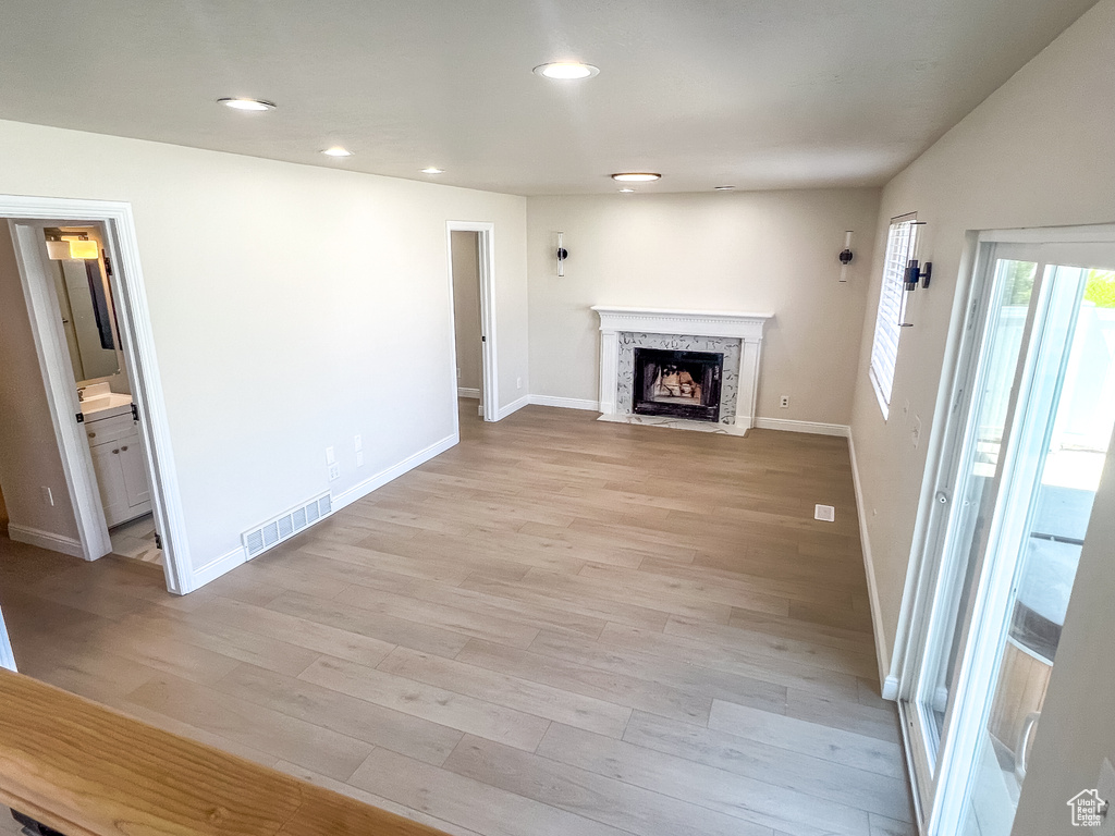 Unfurnished living room with light wood-style floors, a high end fireplace, and recessed lighting