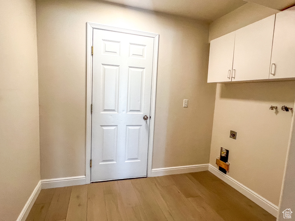 Laundry area featuring electric dryer hookup, light wood finished floors, and cabinet space