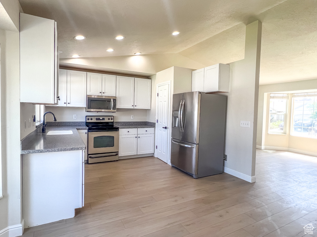 Kitchen featuring stainless steel appliances, lofted ceiling, white cabinets, light wood-type flooring, and recessed lighting