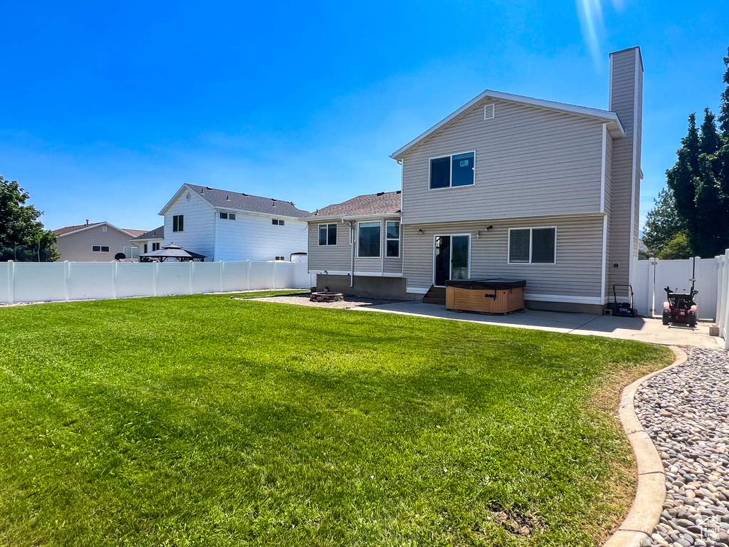 Back of property featuring a hot tub, a patio area, a chimney, and a fenced backyard