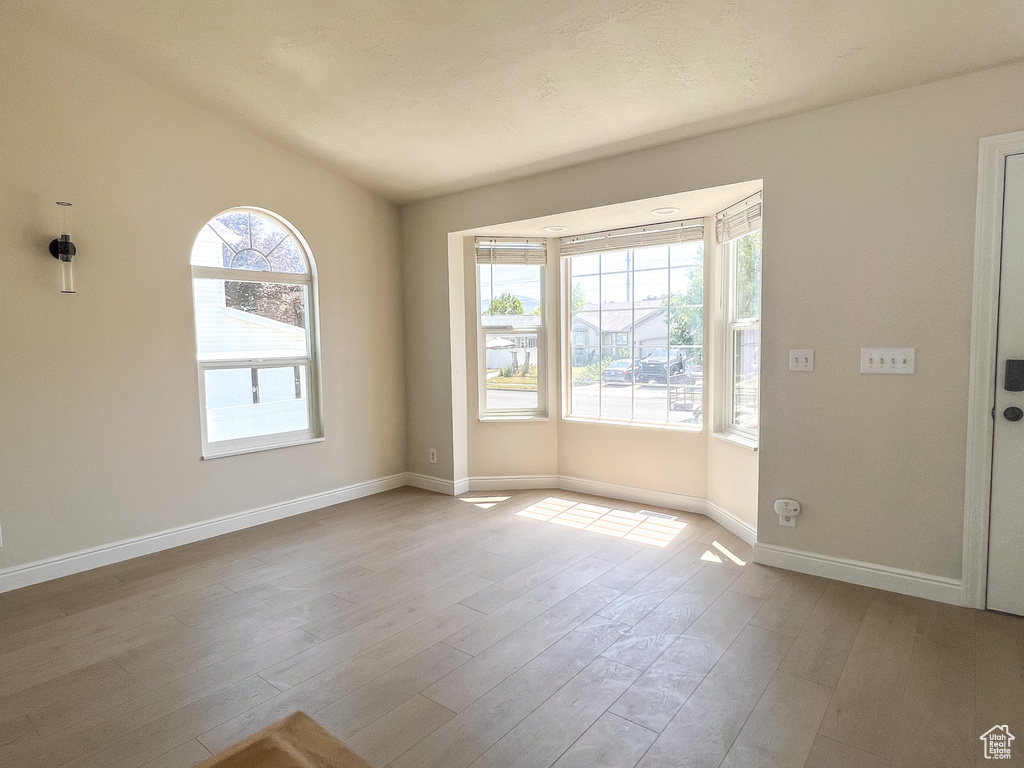Empty room featuring plenty of natural light, wood finished floors, and lofted ceiling