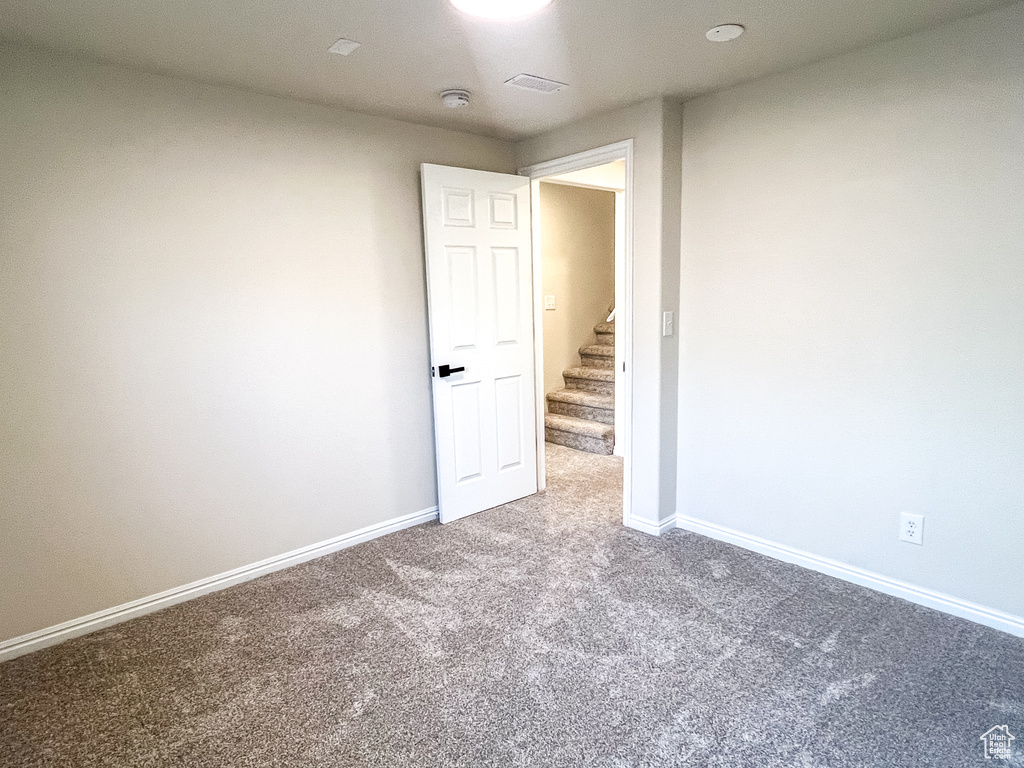 Carpeted empty room featuring stairway and a smoke detector