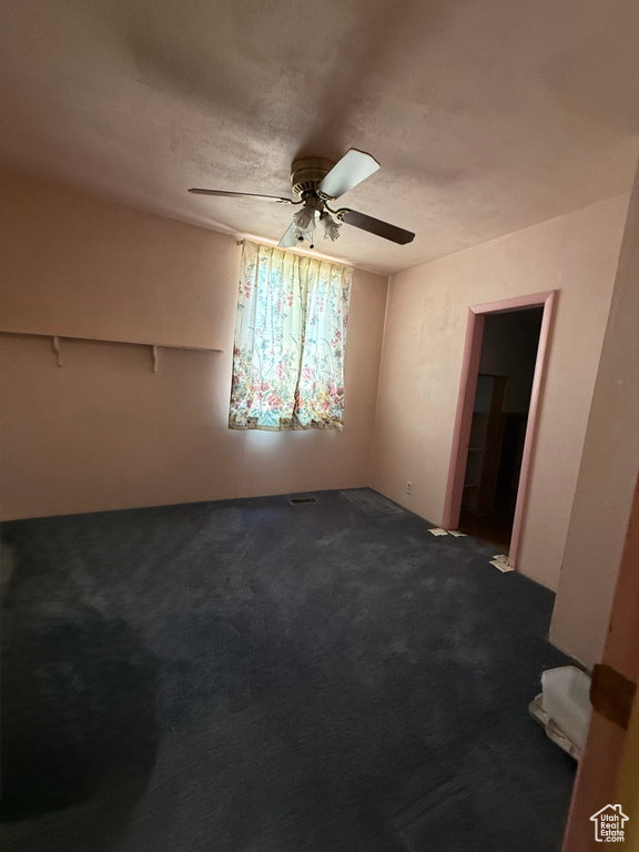 Empty room featuring a ceiling fan, dark carpet, and a textured ceiling