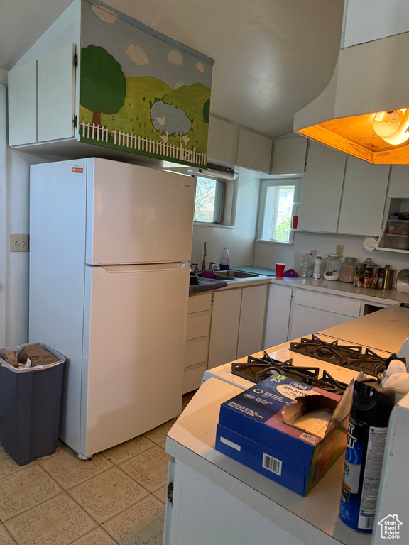 Kitchen with freestanding refrigerator, vaulted ceiling, exhaust hood, light floors, and white cabinets