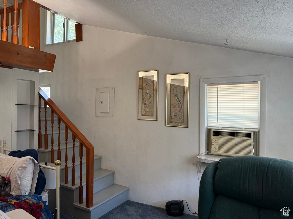 Staircase featuring lofted ceiling, electric panel, carpet, and a textured ceiling