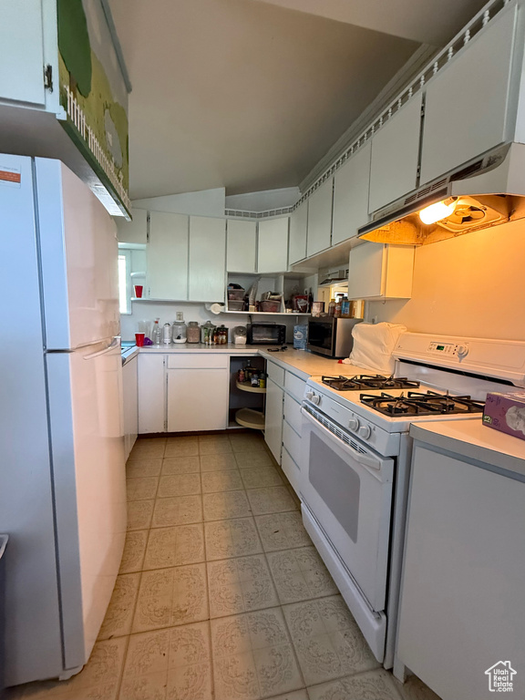 Kitchen featuring white appliances, under cabinet range hood, light countertops, and white cabinets
