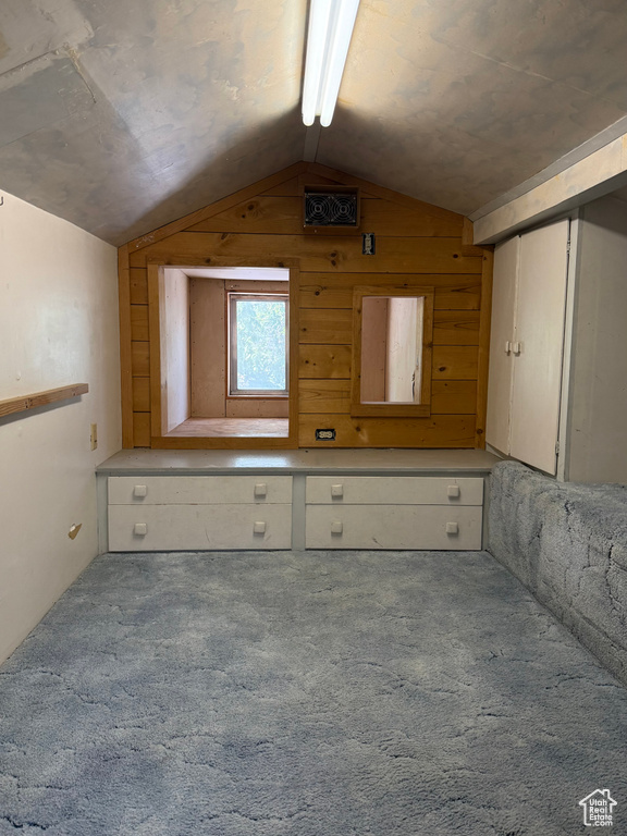 Additional living space featuring vaulted ceiling, carpet, and wood walls