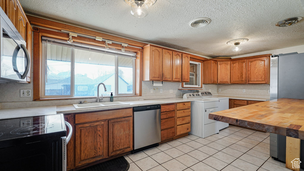 Kitchen with stainless steel appliances, independent washer and dryer, brown cabinets, light tile patterned floors, and wood counters