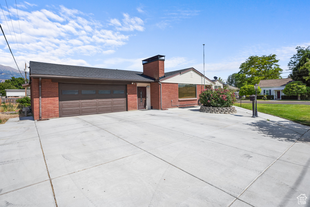 Single story home with brick siding, driveway, an attached garage, a chimney, and a mountain view