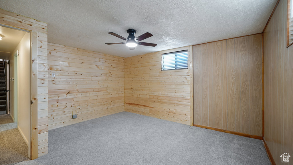 Empty room featuring wood walls, a ceiling fan, carpet floors, a textured ceiling, and stairs