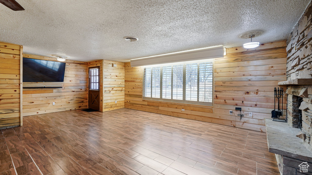 Unfurnished living room featuring a textured ceiling, wooden walls, wood finished floors, and a fireplace