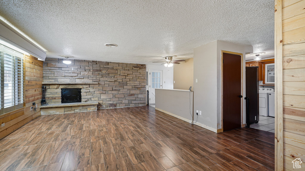 Unfurnished living room featuring washer / clothes dryer, a fireplace, wood finished floors, a ceiling fan, and healthy amount of natural light