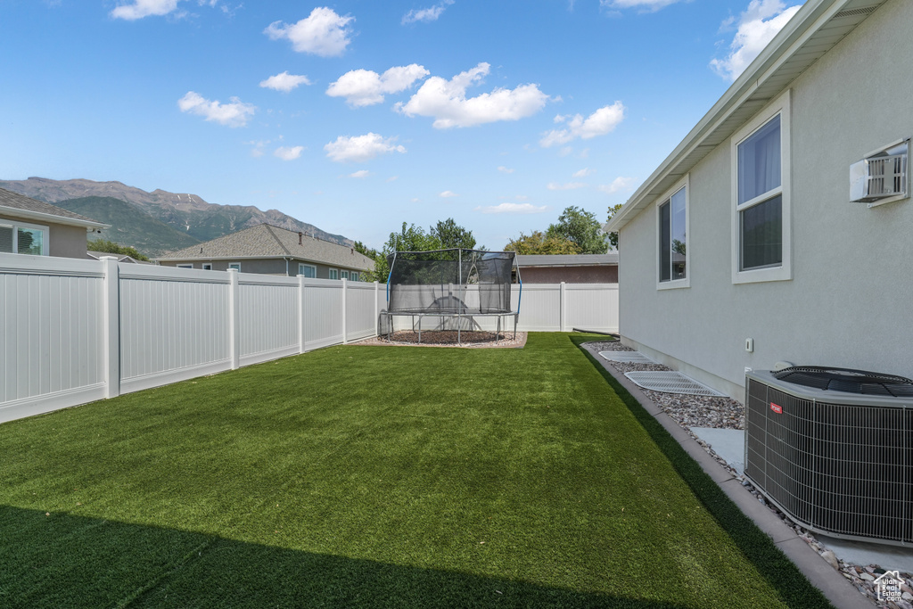 Fenced backyard featuring a trampoline, a mountain view, and a wall mounted air conditioner