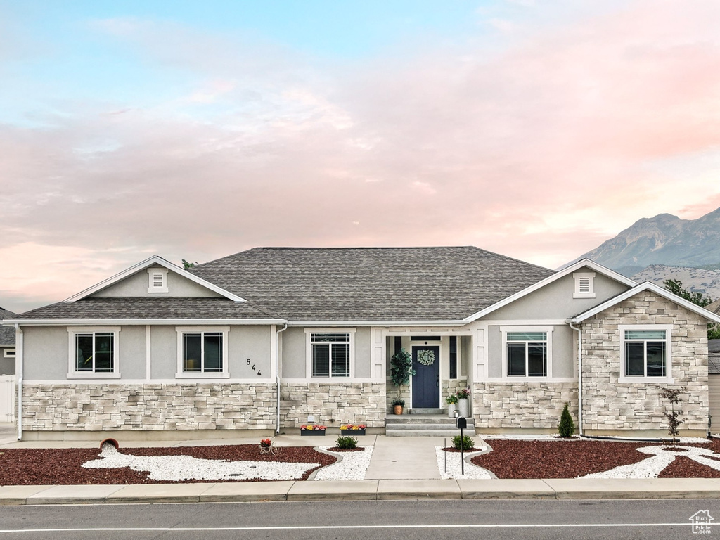 View of front of house featuring stone siding, stucco siding, roof with shingles, and a mountain view