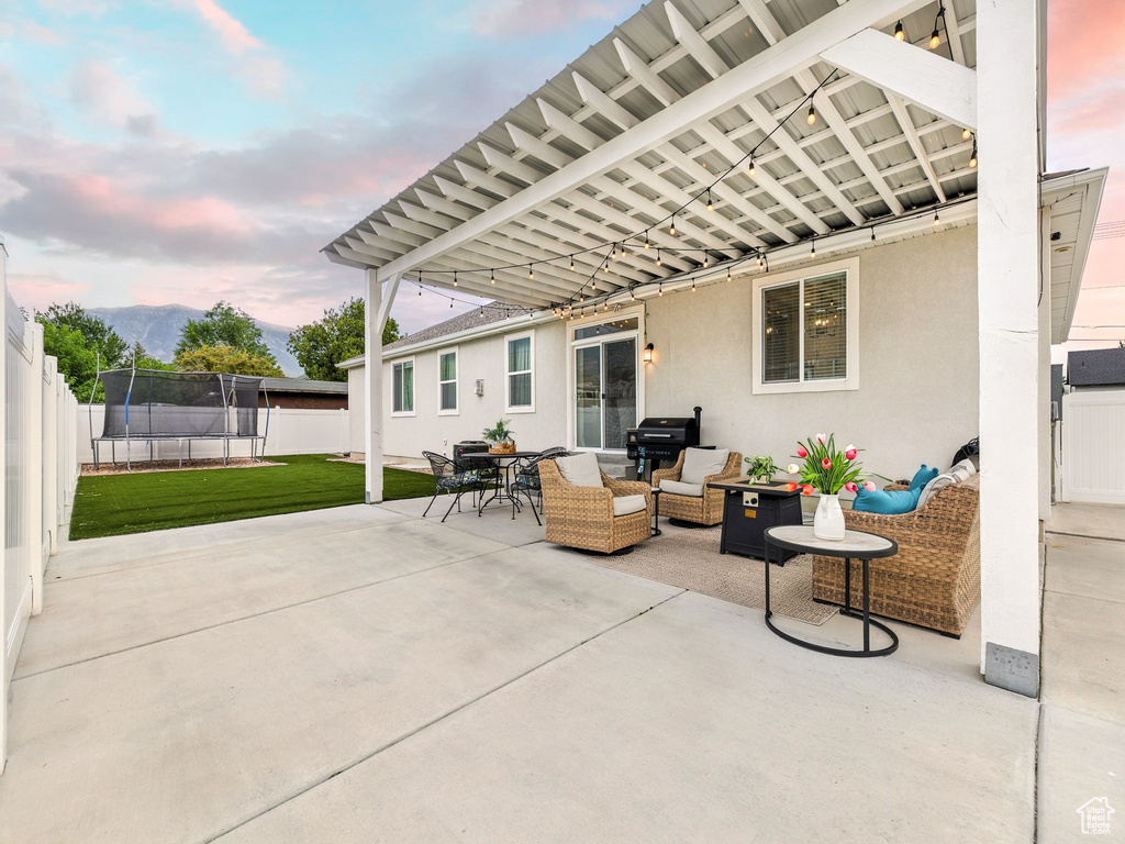 Fenced backyard with a trampoline, a patio, an outdoor living space, and a mountain view