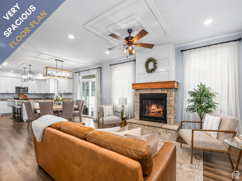 Living area featuring a stone fireplace, a ceiling fan, recessed lighting, dark wood-style flooring, and a chandelier