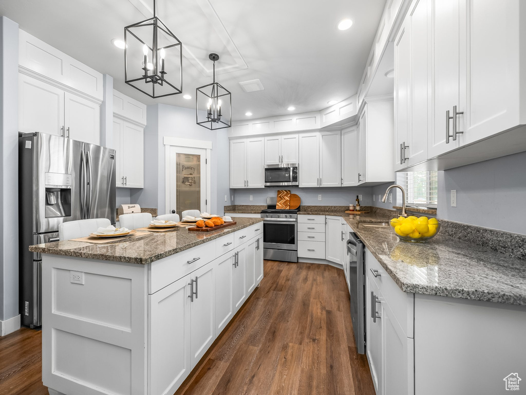 Kitchen with appliances with stainless steel finishes, a kitchen island, recessed lighting, a chandelier, and white cabinetry