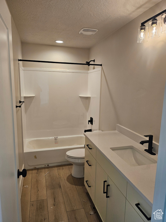 Bathroom with a textured ceiling, vanity,  shower combination, wood finished floors, and recessed lighting