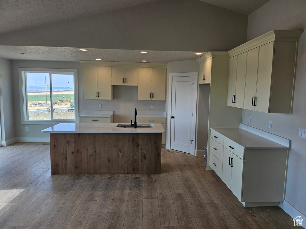 Kitchen featuring a center island with sink, dark wood-style floors, lofted ceiling, white cabinetry, and recessed lighting