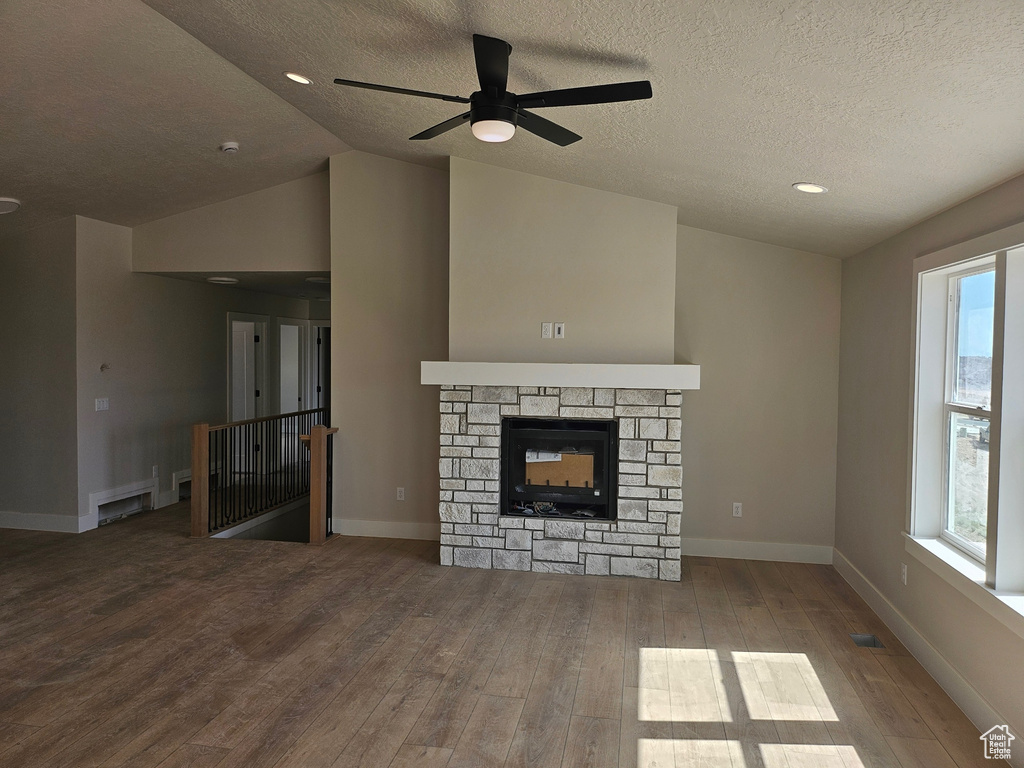 Unfurnished living room with wood finished floors, a textured ceiling, ceiling fan, healthy amount of natural light, and lofted ceiling