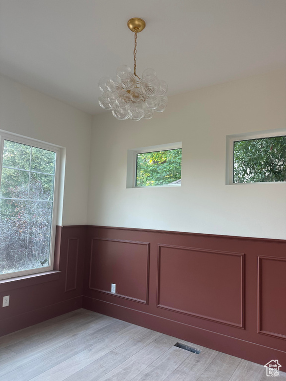 Unfurnished room with a chandelier, a wainscoted wall, a decorative wall, and light wood-style floors