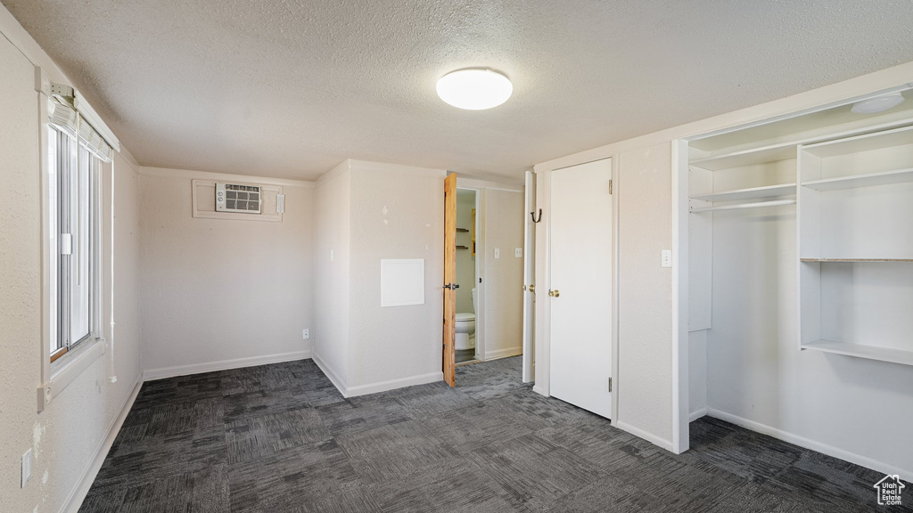 Unfurnished bedroom with a textured ceiling, dark carpet, and a closet