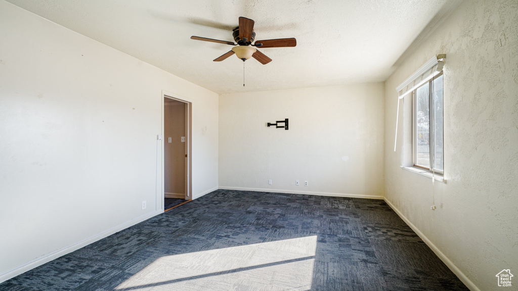 Spare room featuring dark colored carpet and ceiling fan