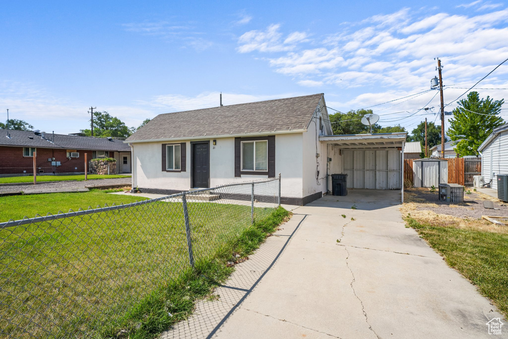View of front of house with stucco siding, driveway, a shingled roof, a carport, and a shed