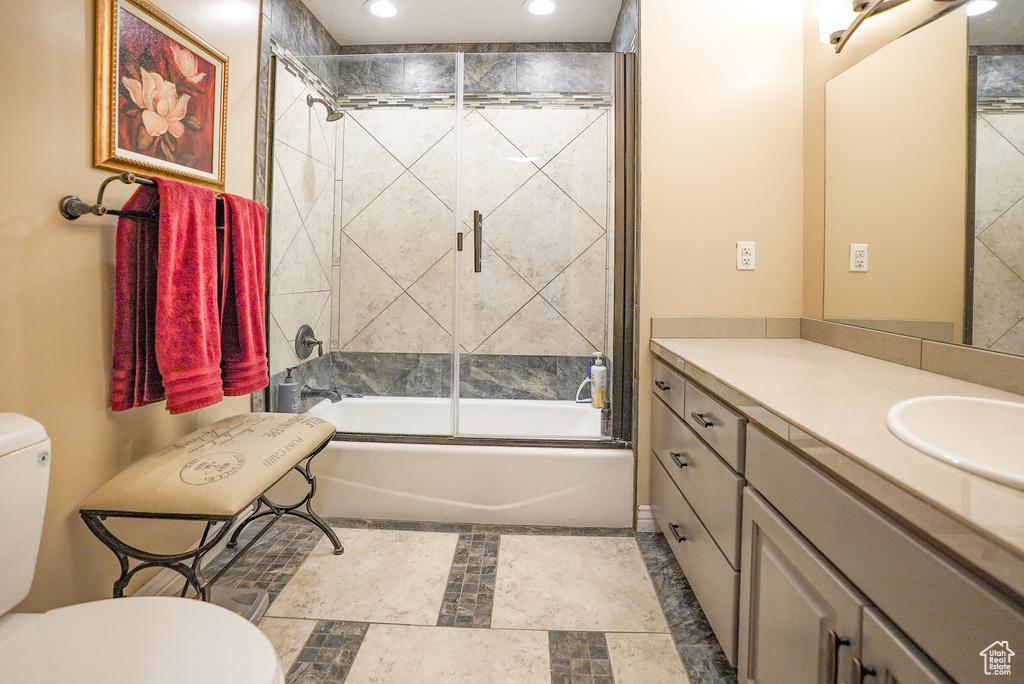 Full bath featuring vanity, enclosed tub / shower combo, recessed lighting, and stone finish floors