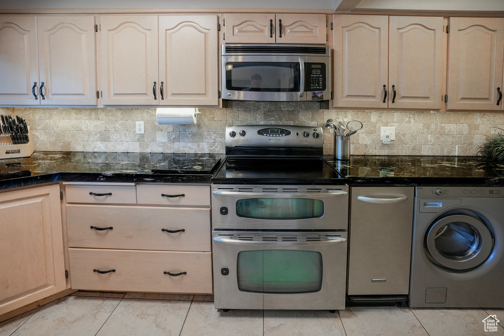 Kitchen with washer / dryer, appliances with stainless steel finishes, backsplash, and dark stone countertops