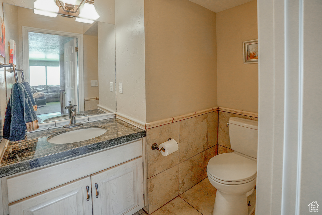 Half bath with vanity, wainscoting, tile walls, and tile patterned floors