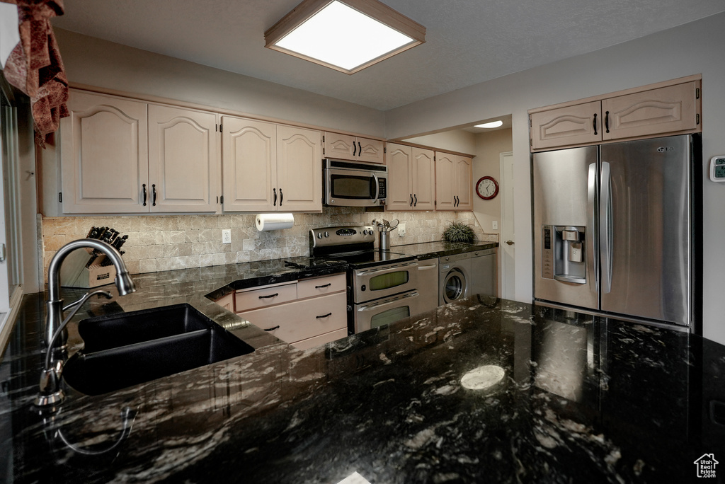 Kitchen featuring appliances with stainless steel finishes, washer / clothes dryer, decorative backsplash, and dark stone counters
