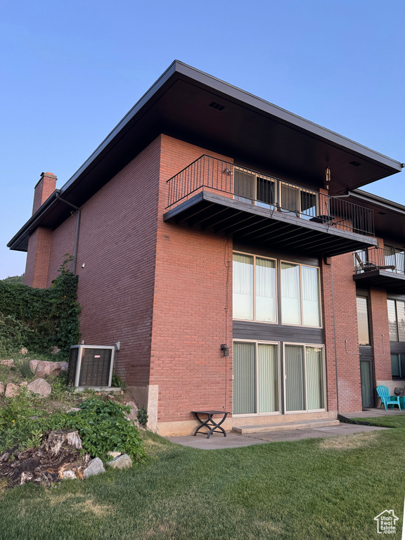 Rear view of house featuring a balcony, brick siding, a chimney, and a lawn