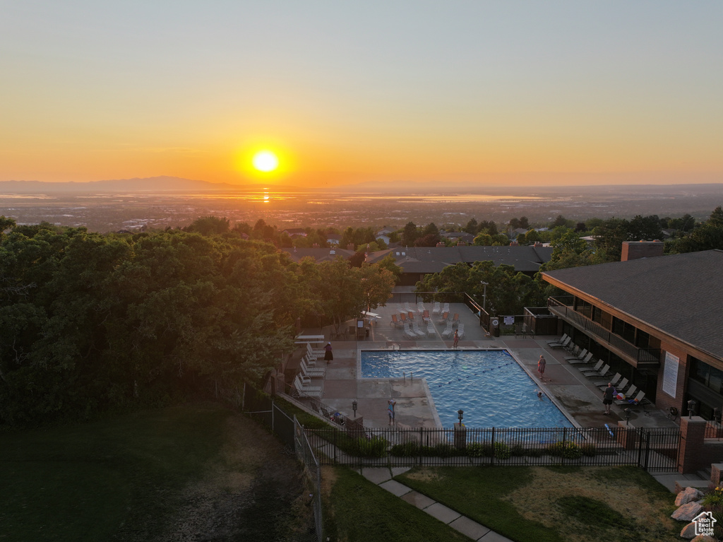 Pool at dusk featuring a fenced backyard, a patio area, and a community pool