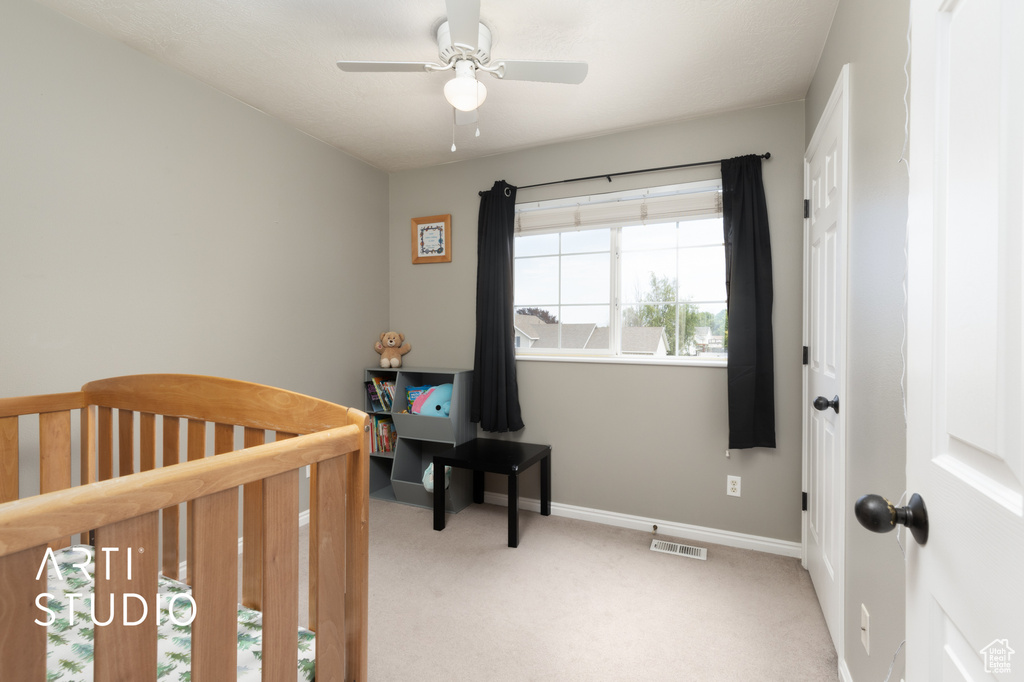 Bedroom featuring light colored carpet, a nursery area, and ceiling fan