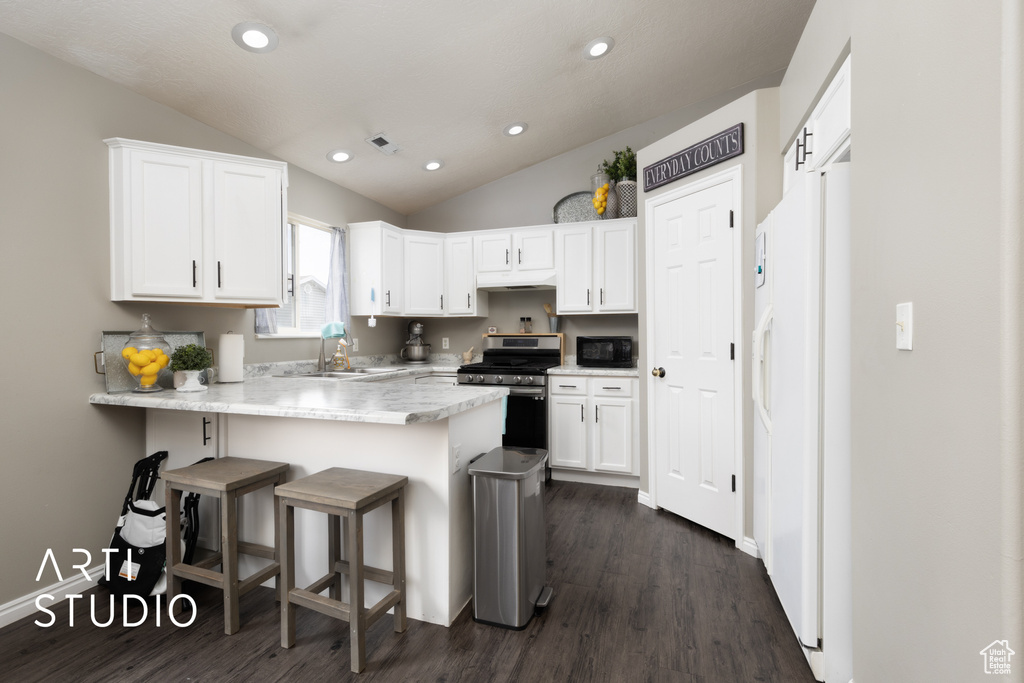 Kitchen featuring white fridge with ice dispenser, stainless steel gas range, black microwave, a peninsula, and white cabinetry