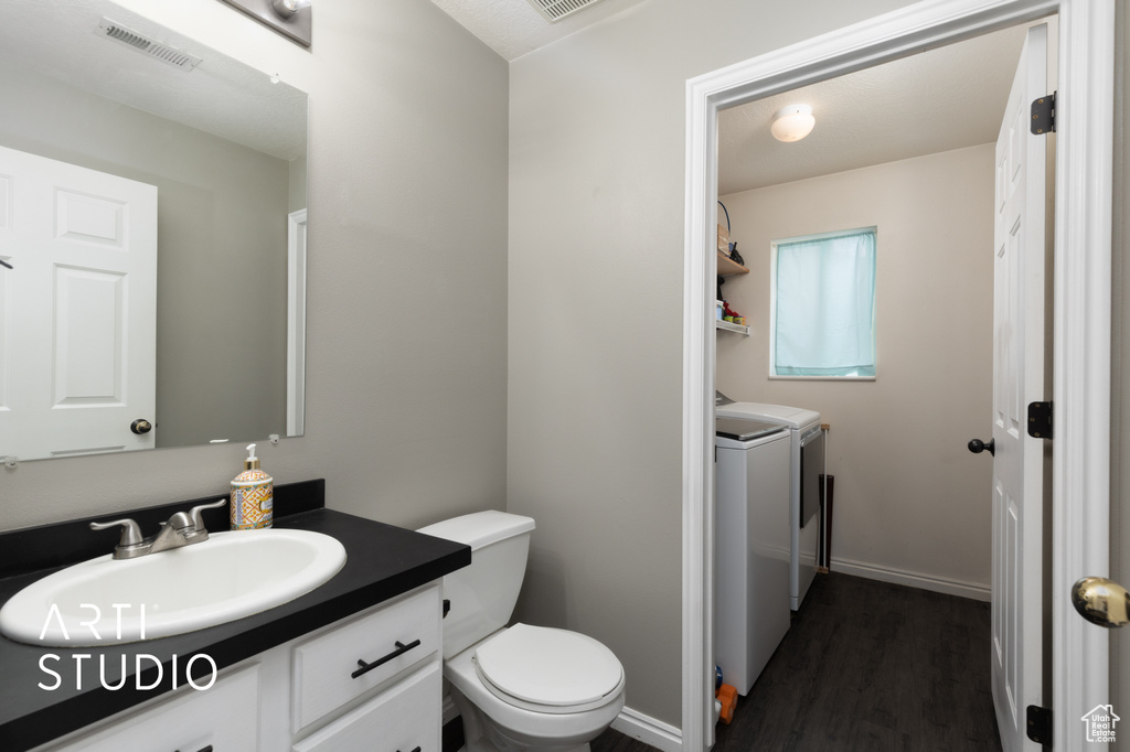 Half bath with washing machine and clothes dryer, vanity, and wood finished floors