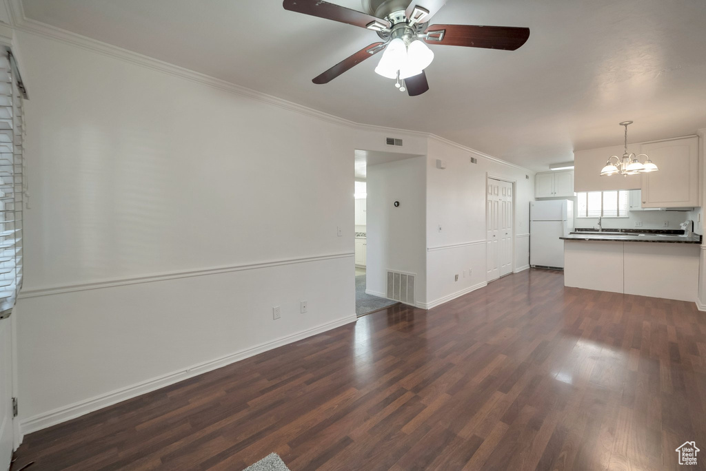 Unfurnished living room featuring a chandelier, dark wood-style floors, ornamental molding, and ceiling fan