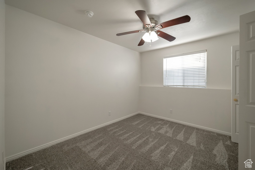 Empty room featuring dark carpet, a ceiling fan, and a smoke detector