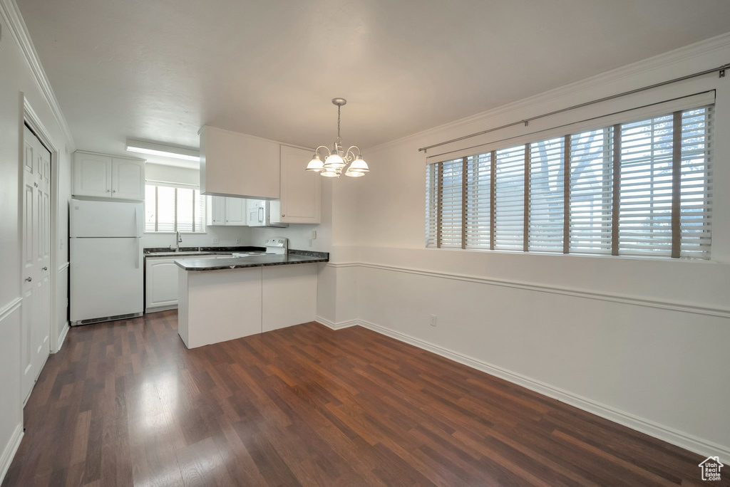 Kitchen featuring white appliances, dark countertops, a chandelier, a peninsula, and dark wood finished floors